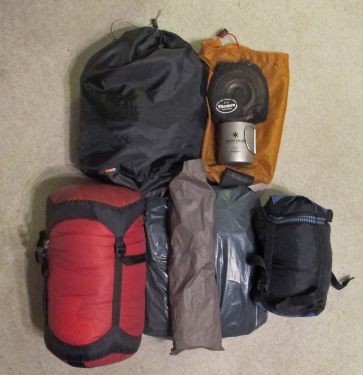L to R top: Food bag, cook pot, Esbit stove, cup L to R bottom: sleeping bag, mattress, tent poles and tent.  